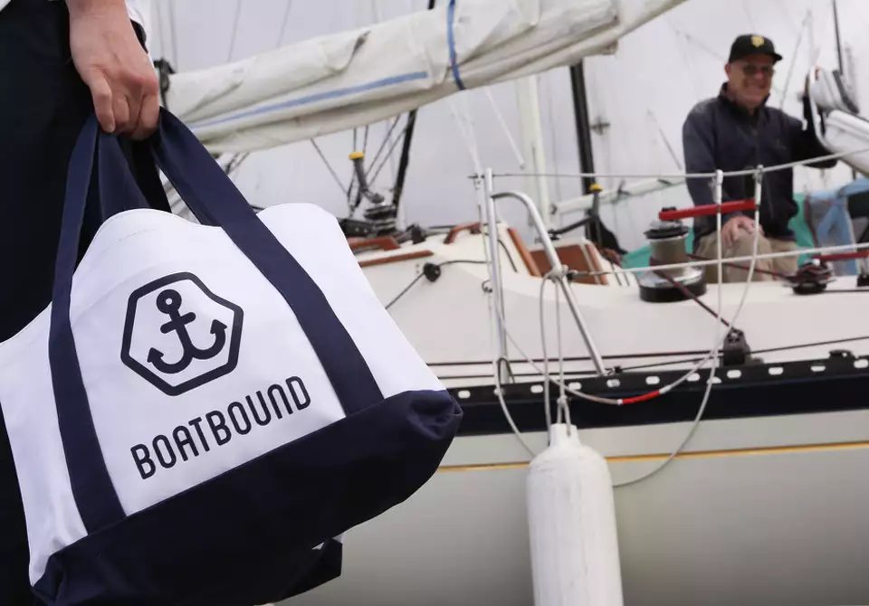 Boatbound-branded tote bag beside a sailboat